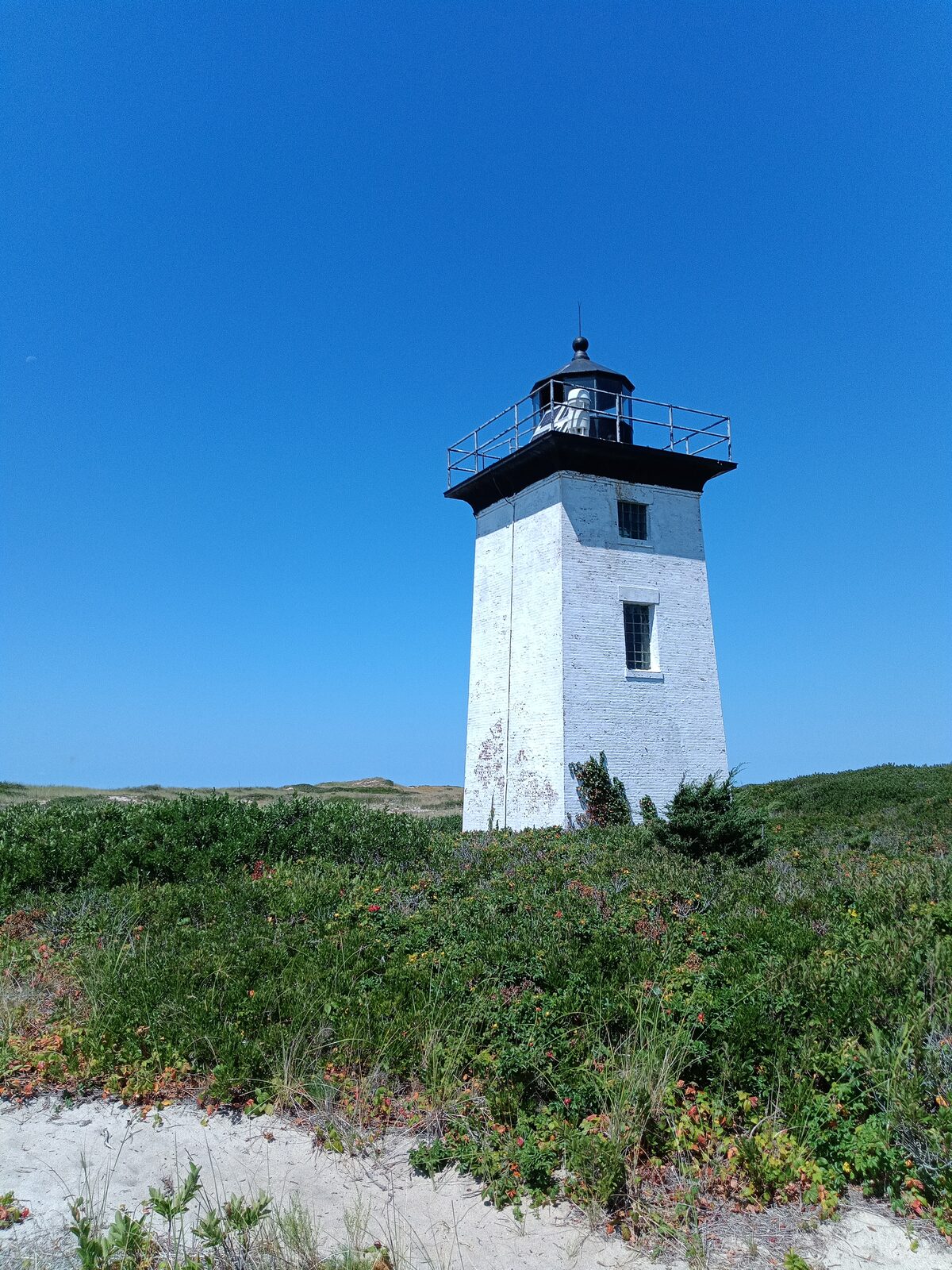 A white brick lighthouse on a dune under a clear blue sky, taken with the HiBreak Pro