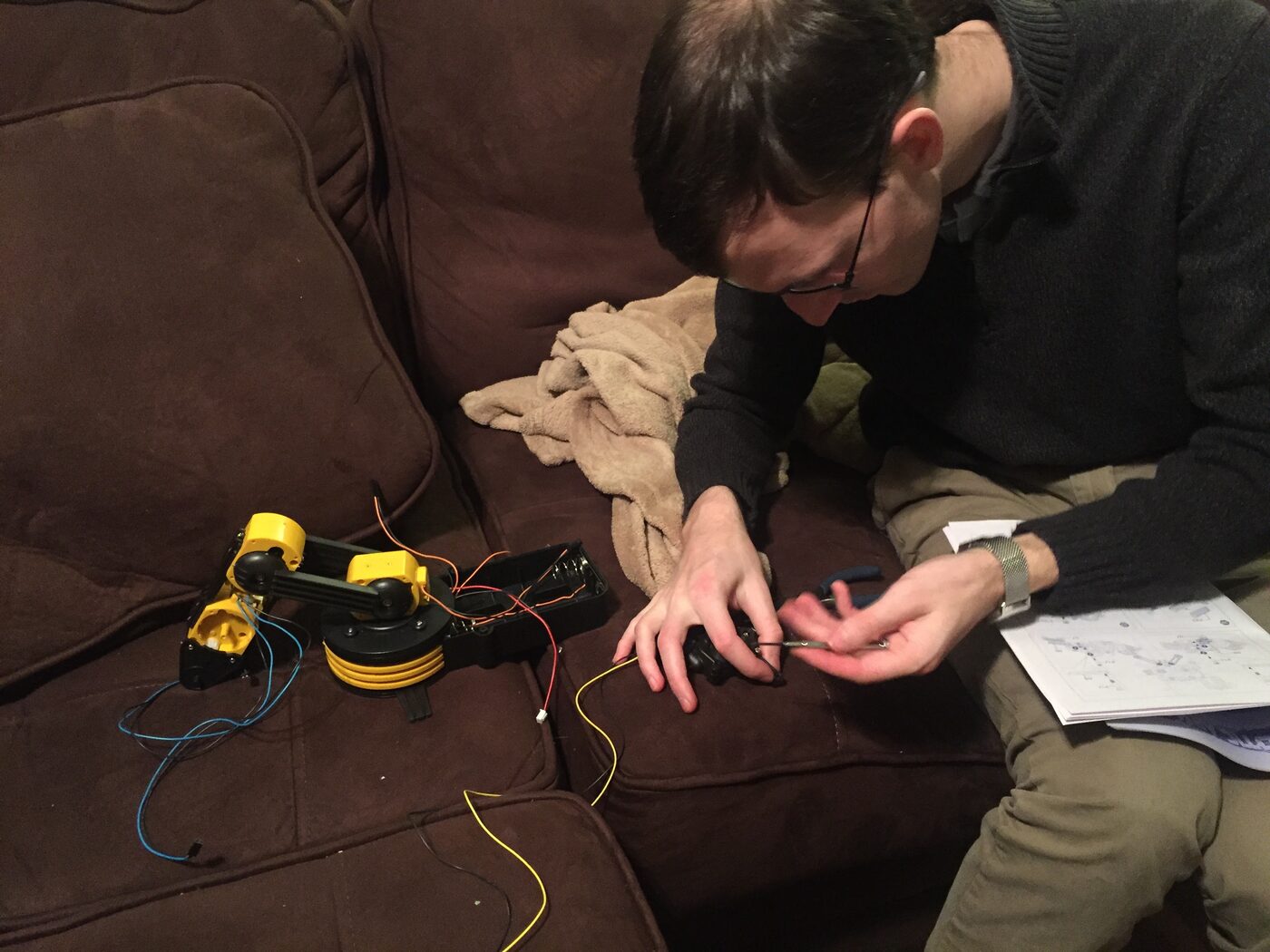 My brother assembling the robotic arm kit on the couch, following the instruction manual