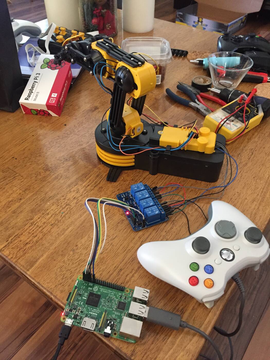 The bench: the arm, a four-channel relay board, the Raspberry Pi 3, a multimeter, and the Xbox controller